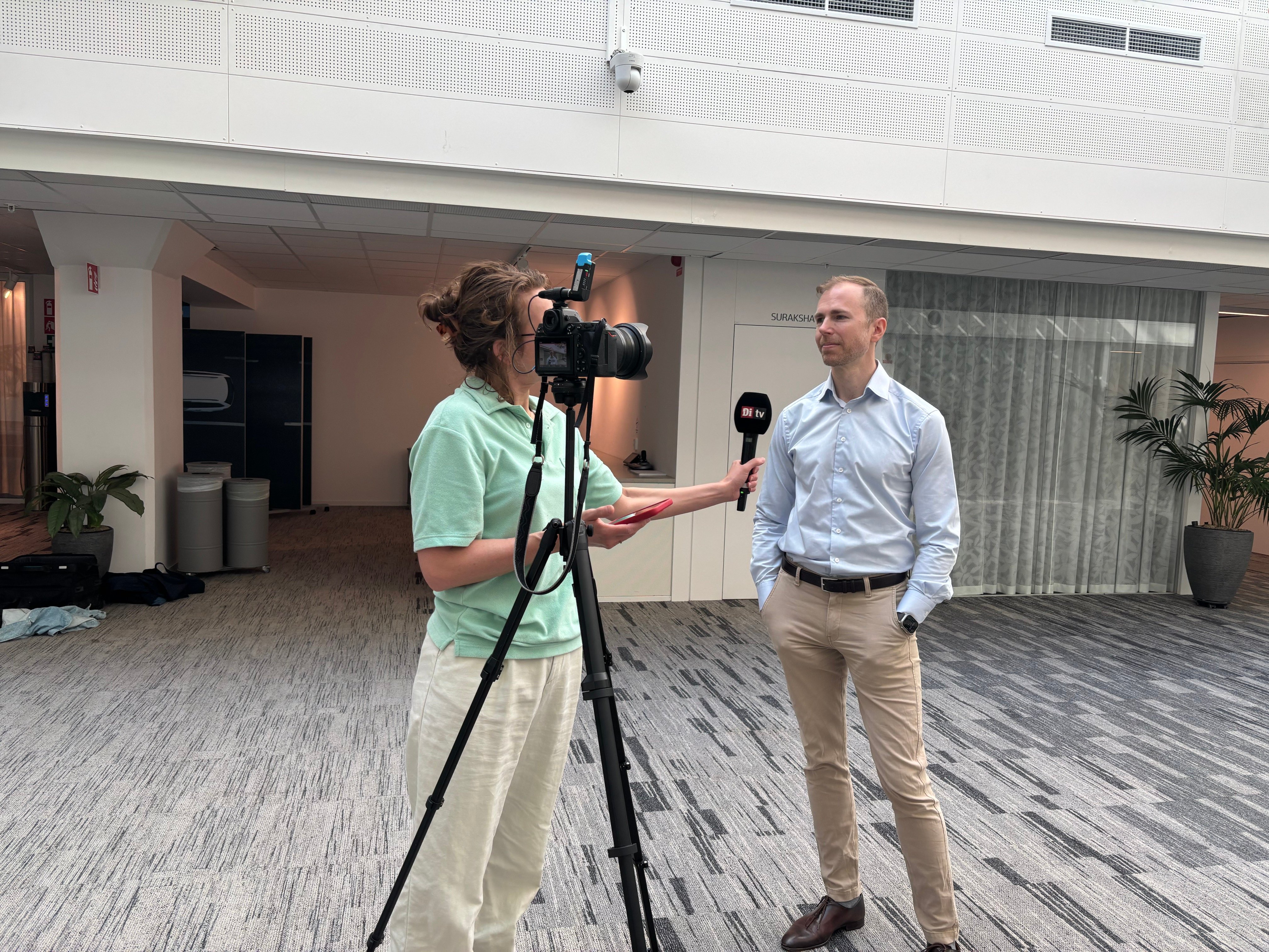 Jonas Lundin standing in front of a camera, being interviewed by a Di reporter holding a camera.
